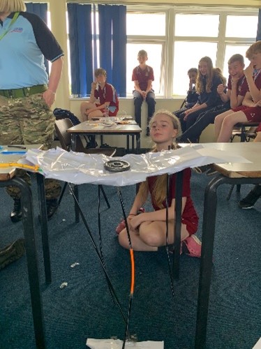 Image shows school pupils testing their bridges across two tables, with RAF STEM Ambassadors.