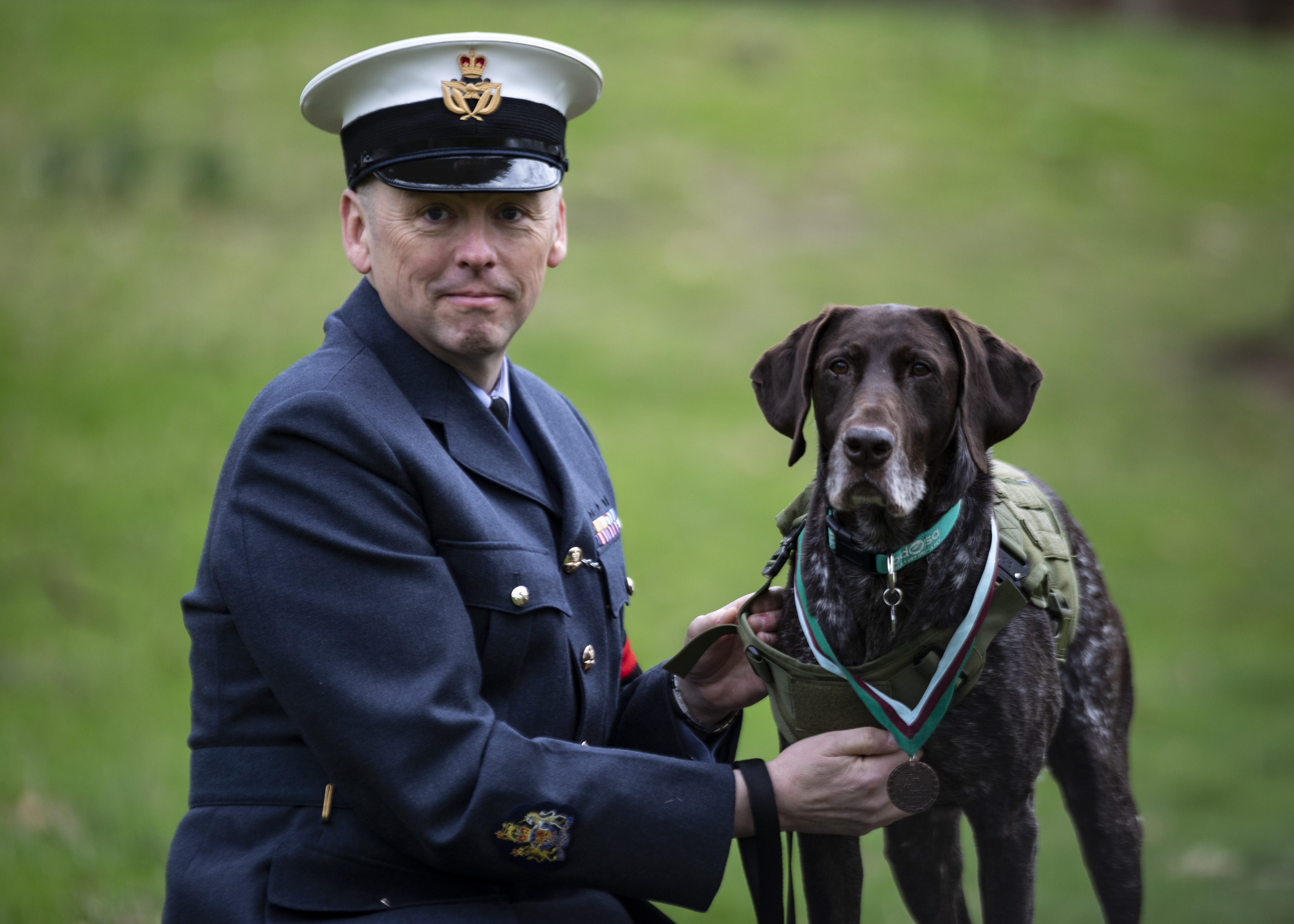 Personnel kneels with dog wearing medal.