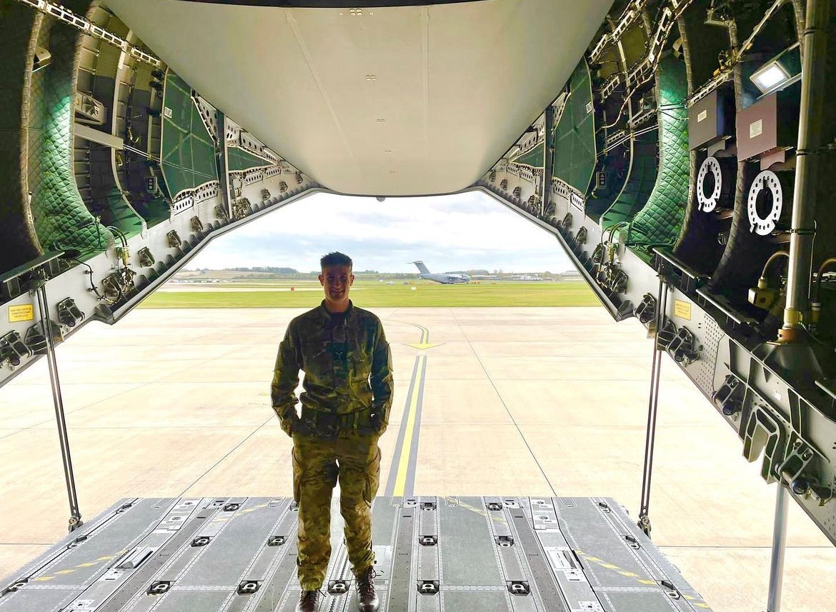 Image shows RAF aviator standing on the open cargo holding bay of a carrier aircraft on the airfield.