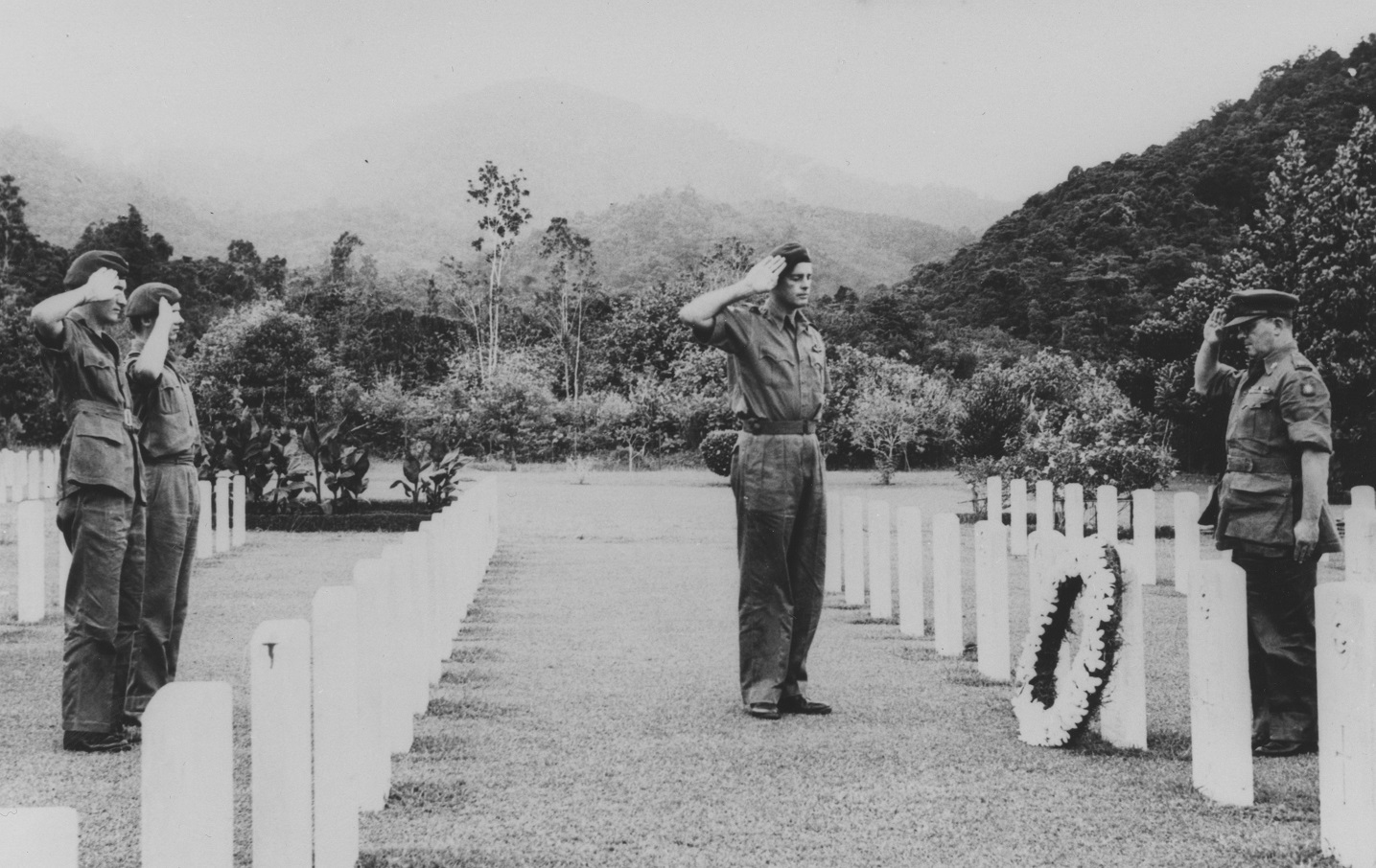 Black and white image shows RAF personnel saluting a wreath and gravestones in a cemetery.