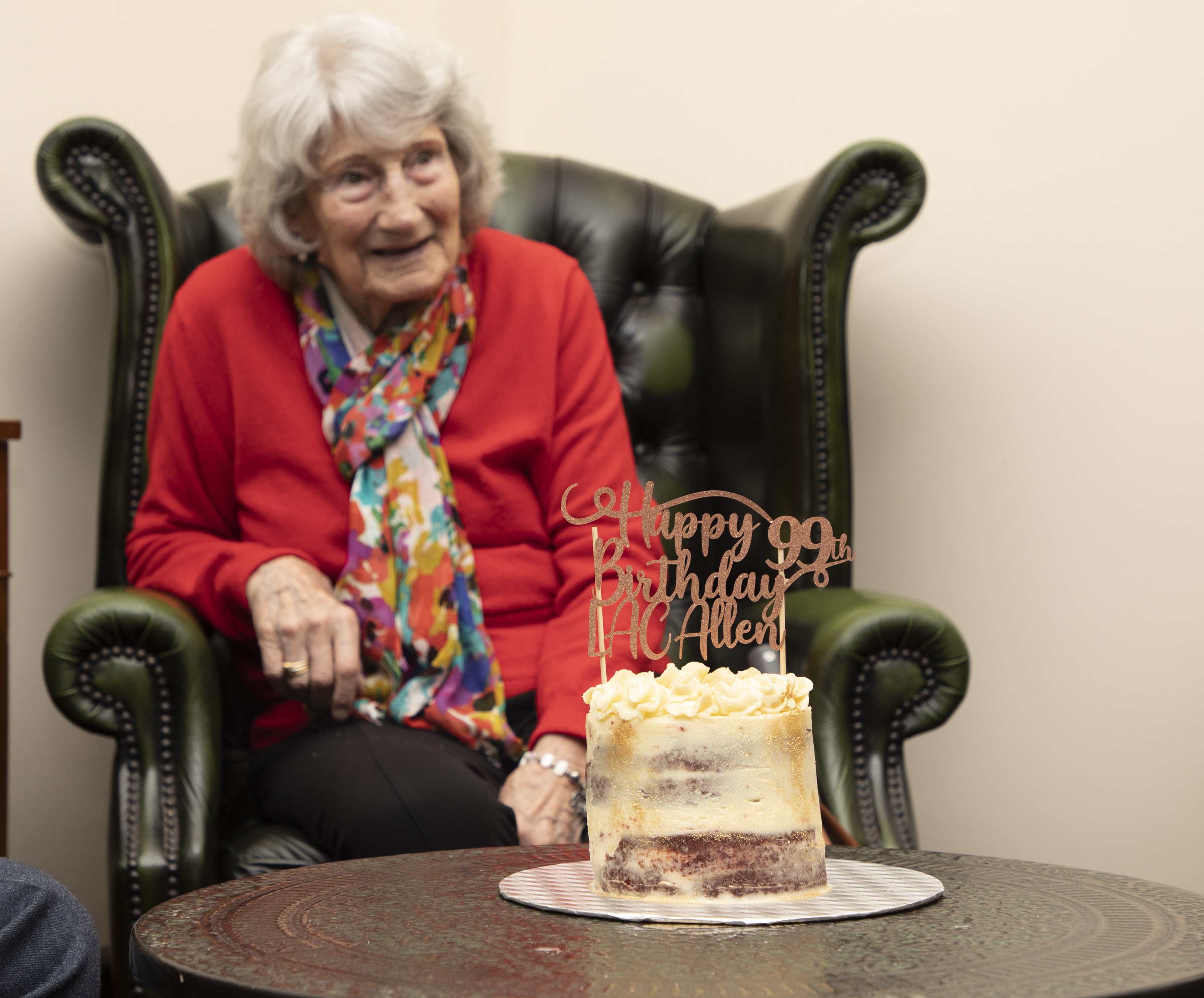 Image shows Veteran sitting in an armchair with birthday cake on table.