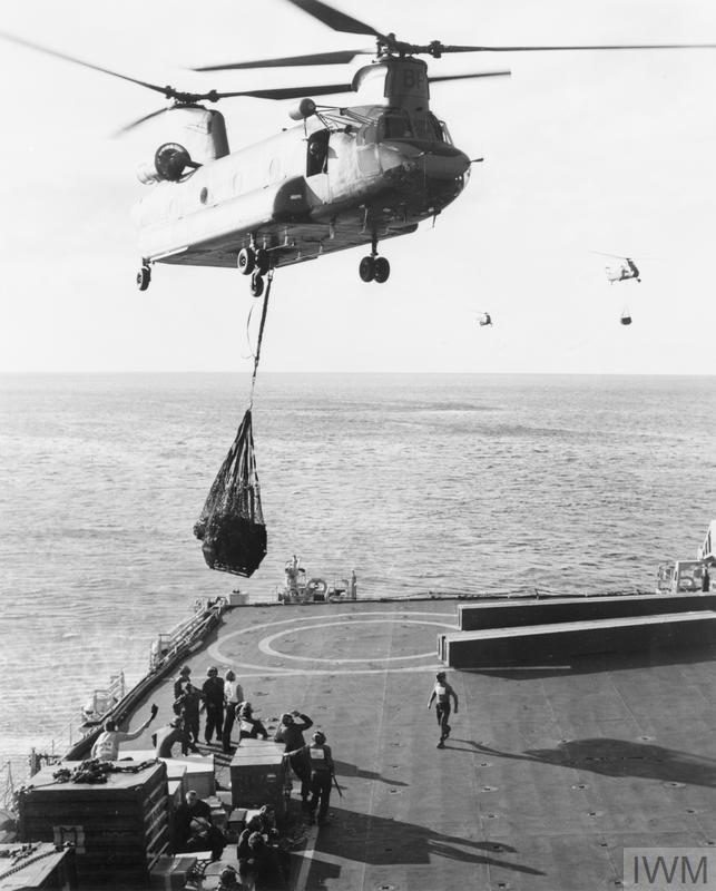 Aged image of a helicopter carrying loaded sling to the deck of a warship.