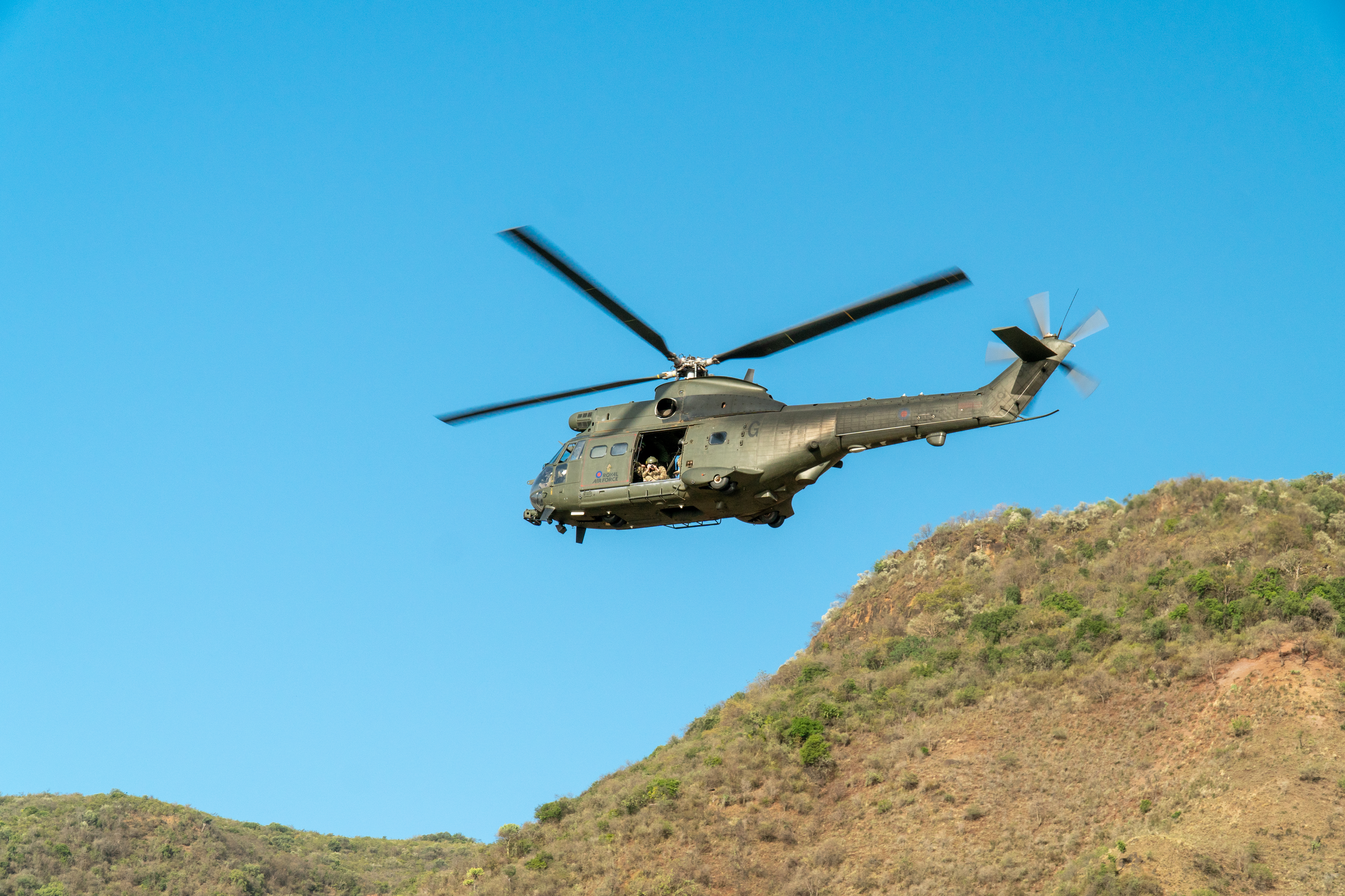 A puma flies in front of the hill tops in front of a clear blue sky