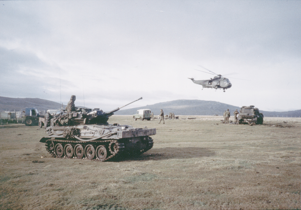Old photo of a helicopter, tanks and personnel in the Falklands.