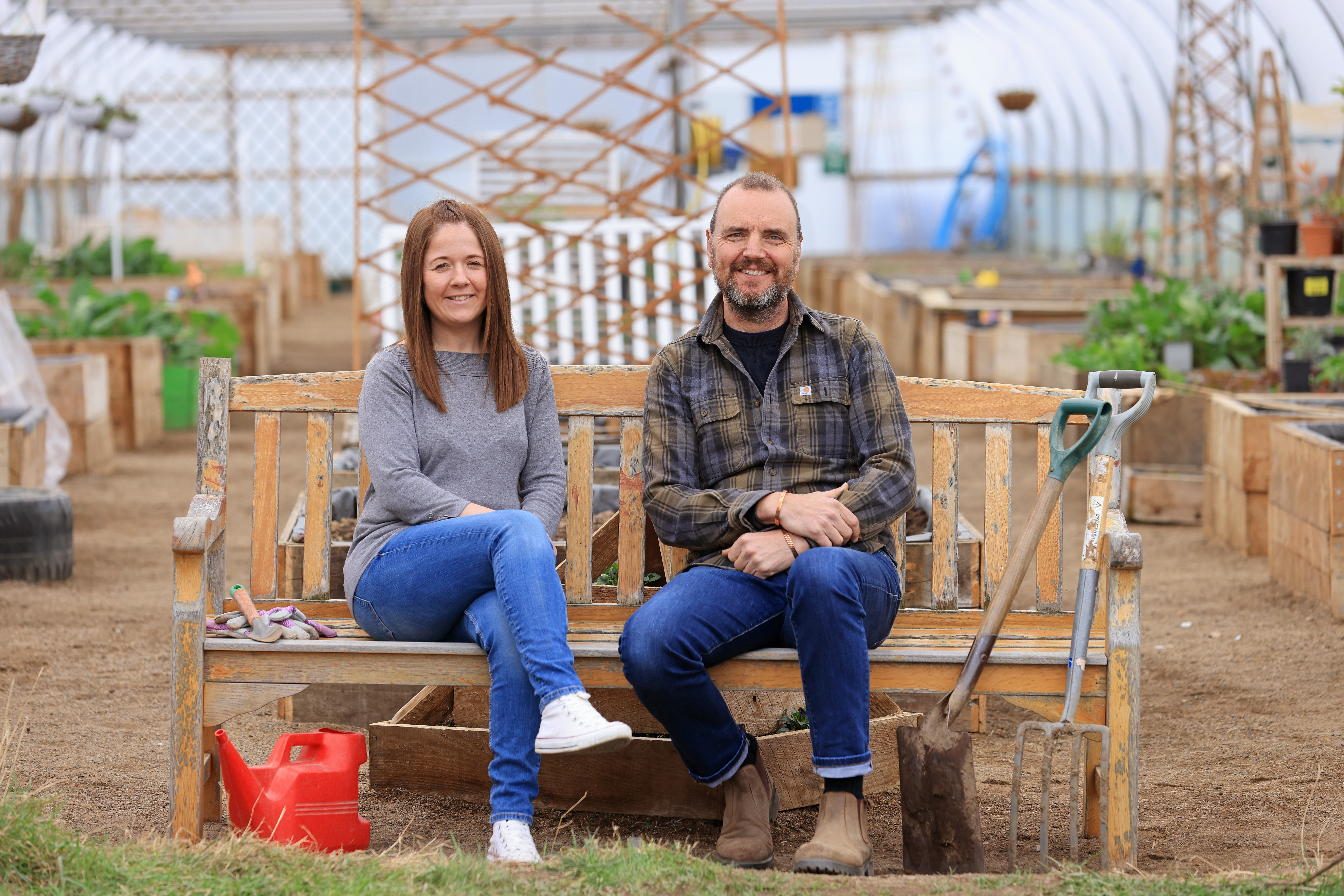 John and Amileigh sit on a bench with gardening tools.