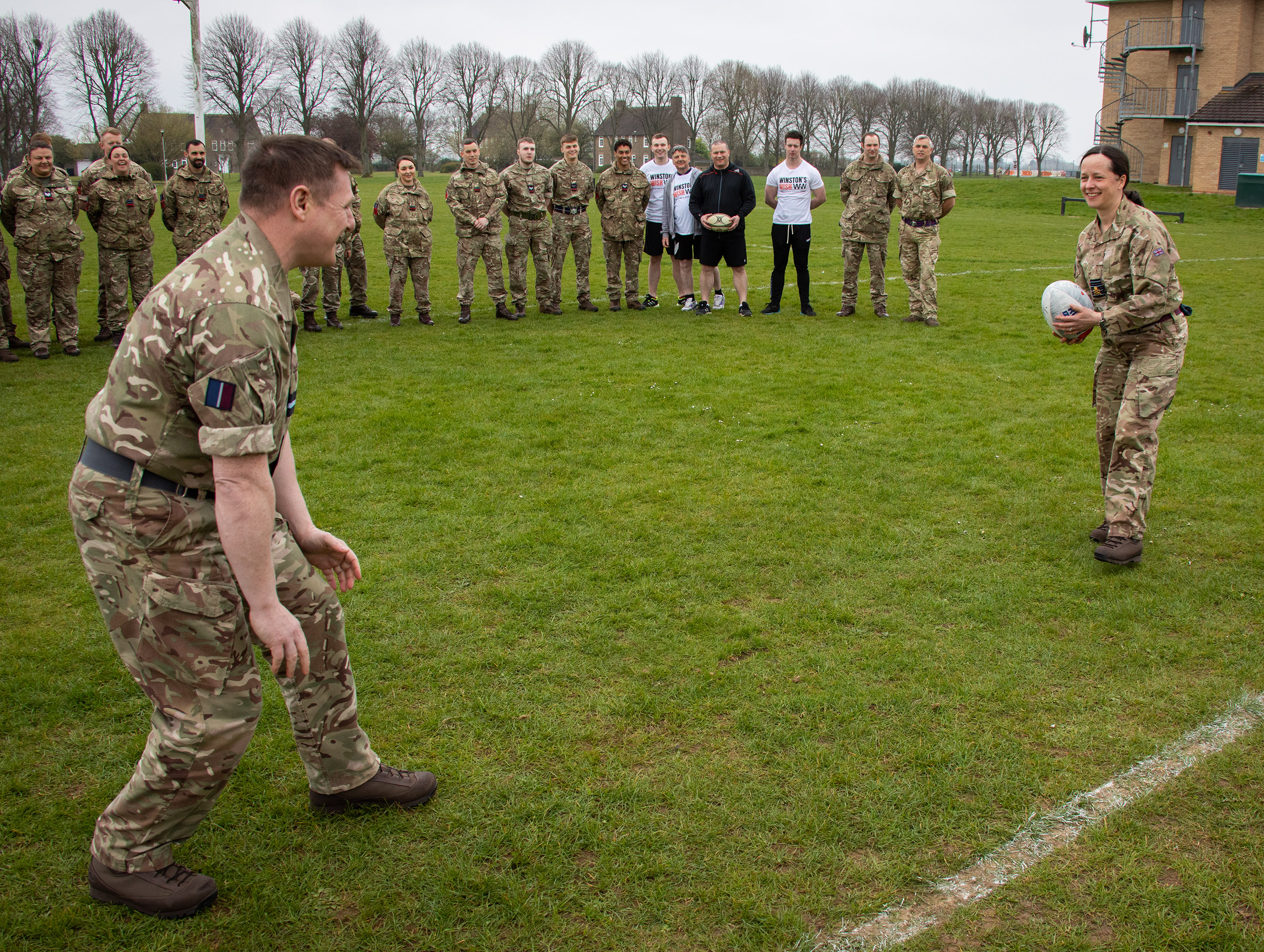 Personnel holds rugby ball to other.