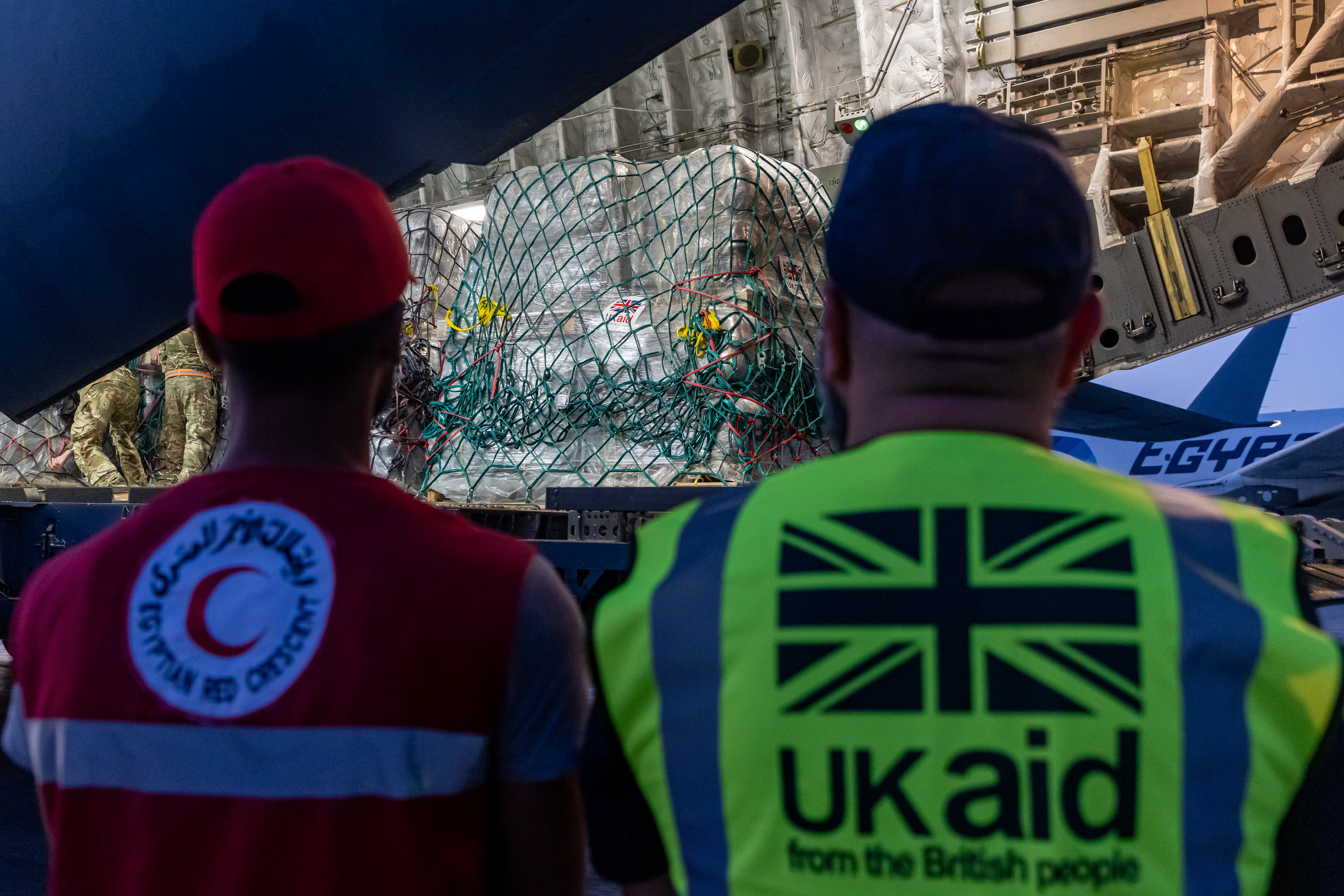 a UK aid person and Egyptian Red Crescent person watching as supplies are unloaded from the C-17 aircraft