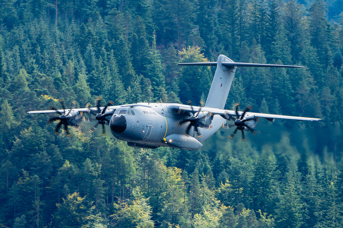 A400M aircraft flying against a backdrop of pine trees