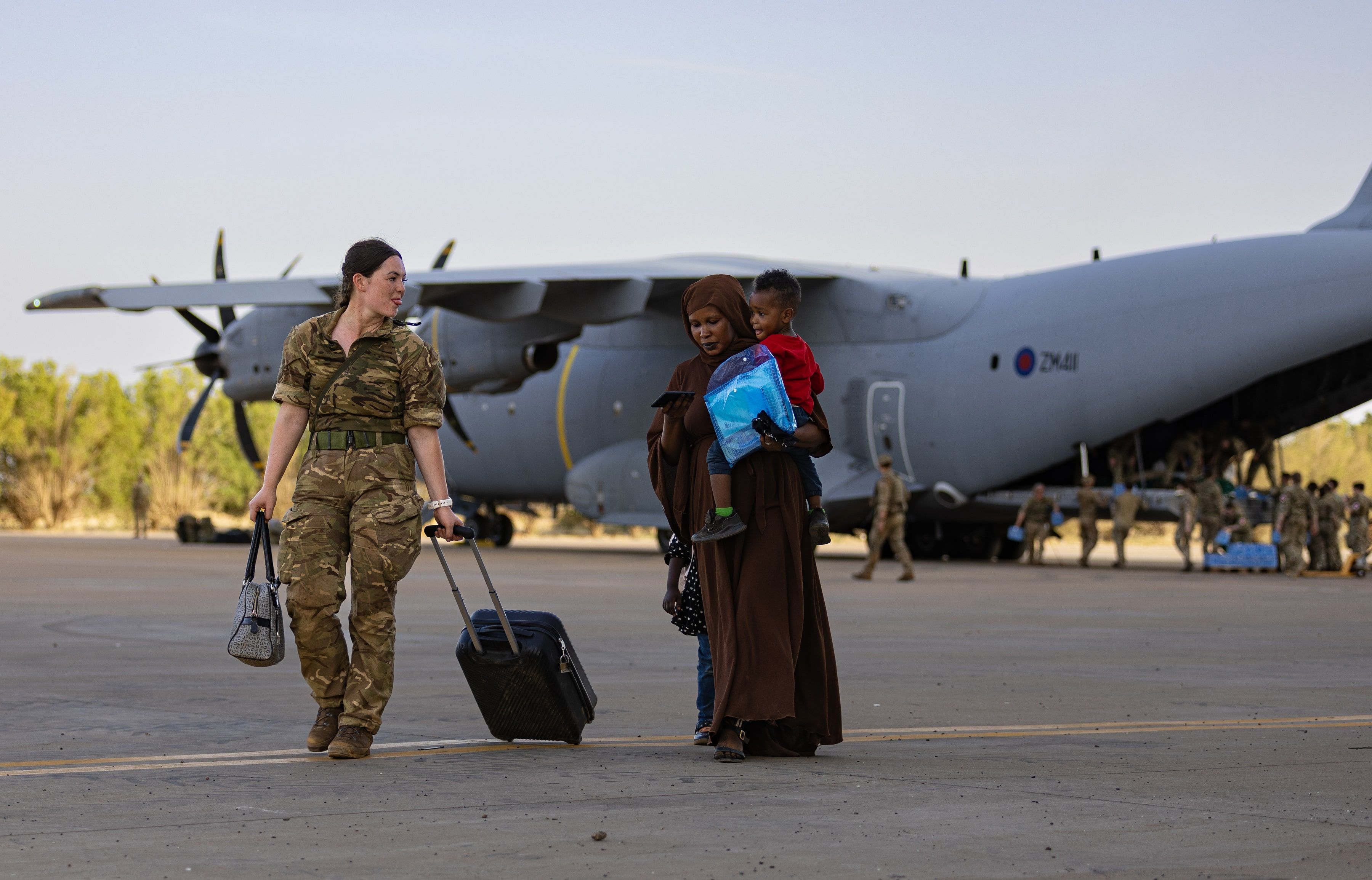 RAF personnel assisting refugee off the plane, sticking out tongue with the little boy in mother's arms. 