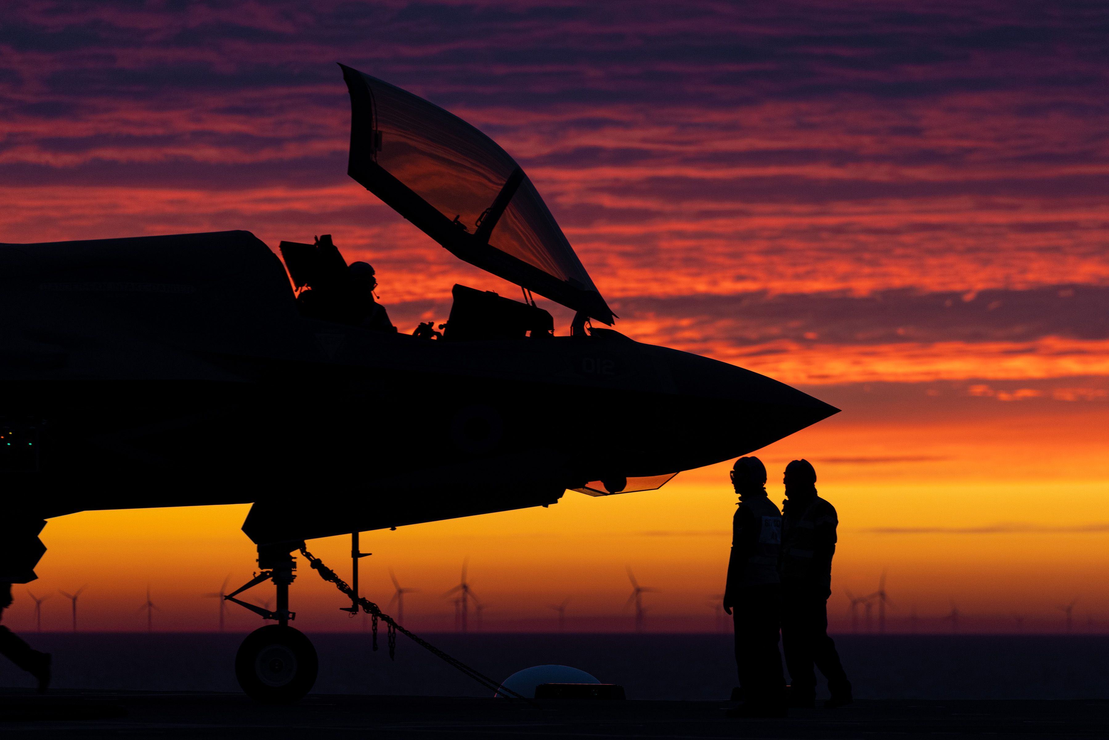 F-35B silhoetted against a sunset background with 2 people standing at the nose