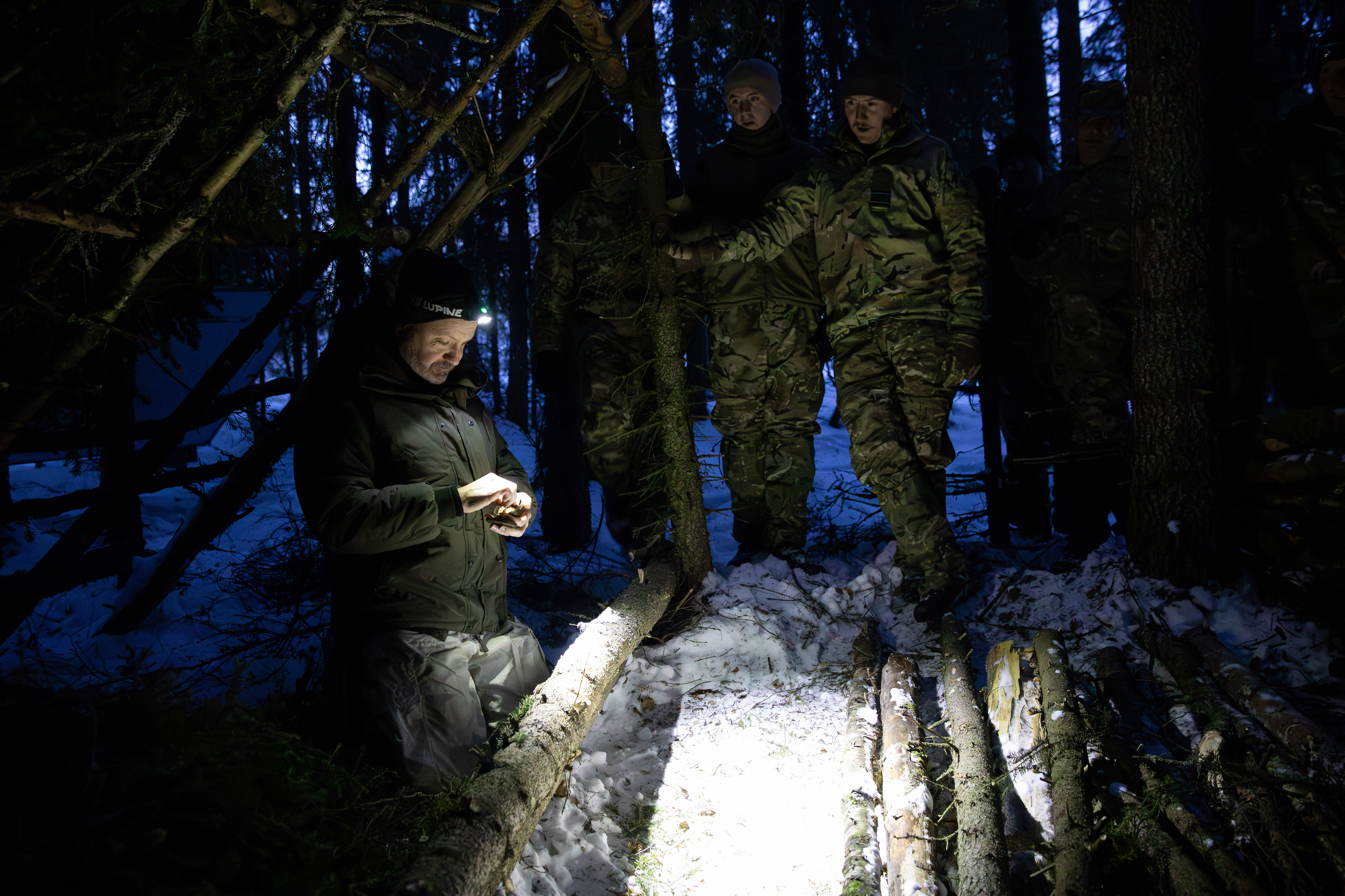 RAF personnel receiving instructions on lighting a fire in a shelter in a snow covered environment