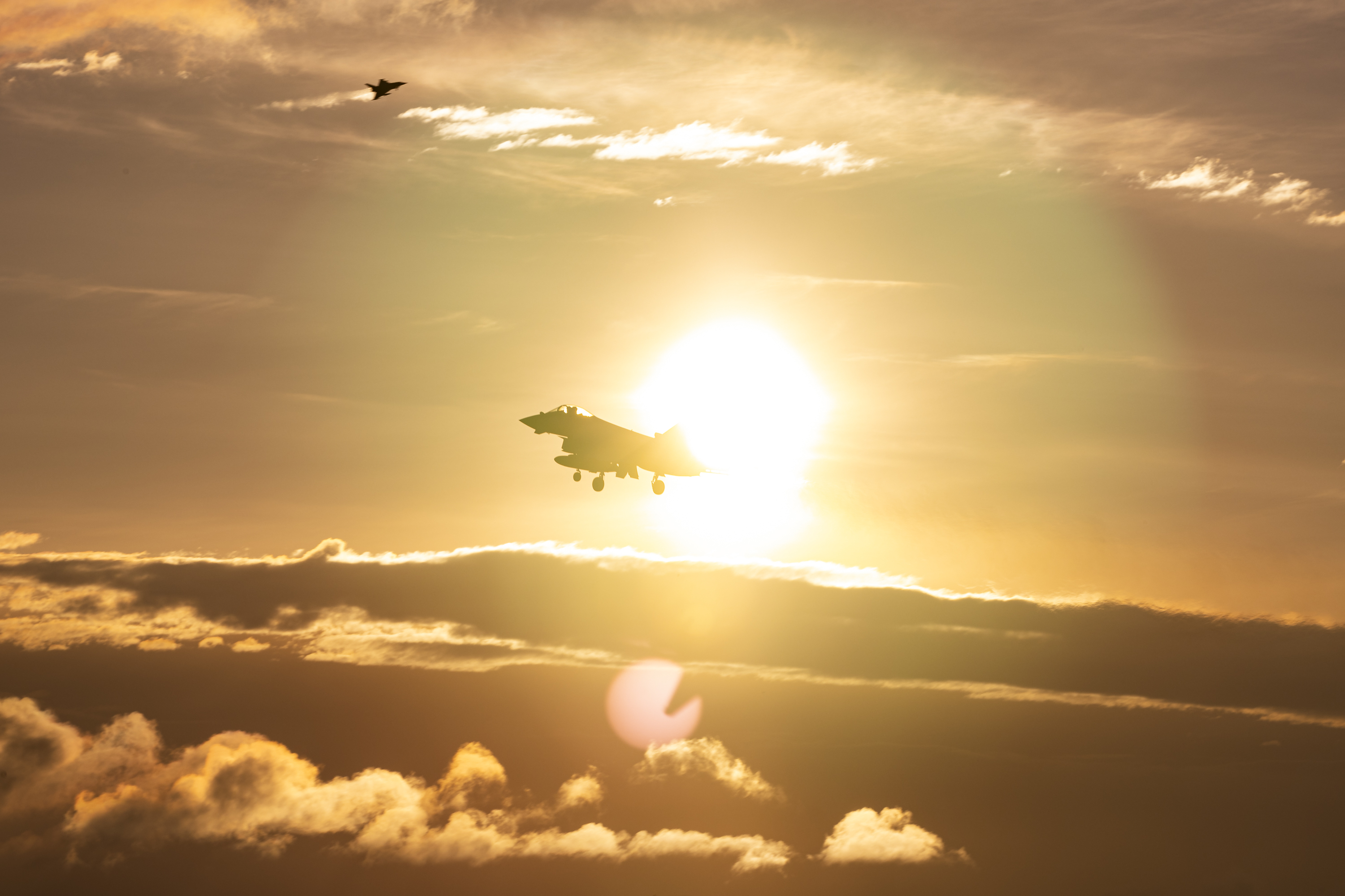 RAF Typhoon aircraft flying against a sunset sky, with a distant Typhoon in the background