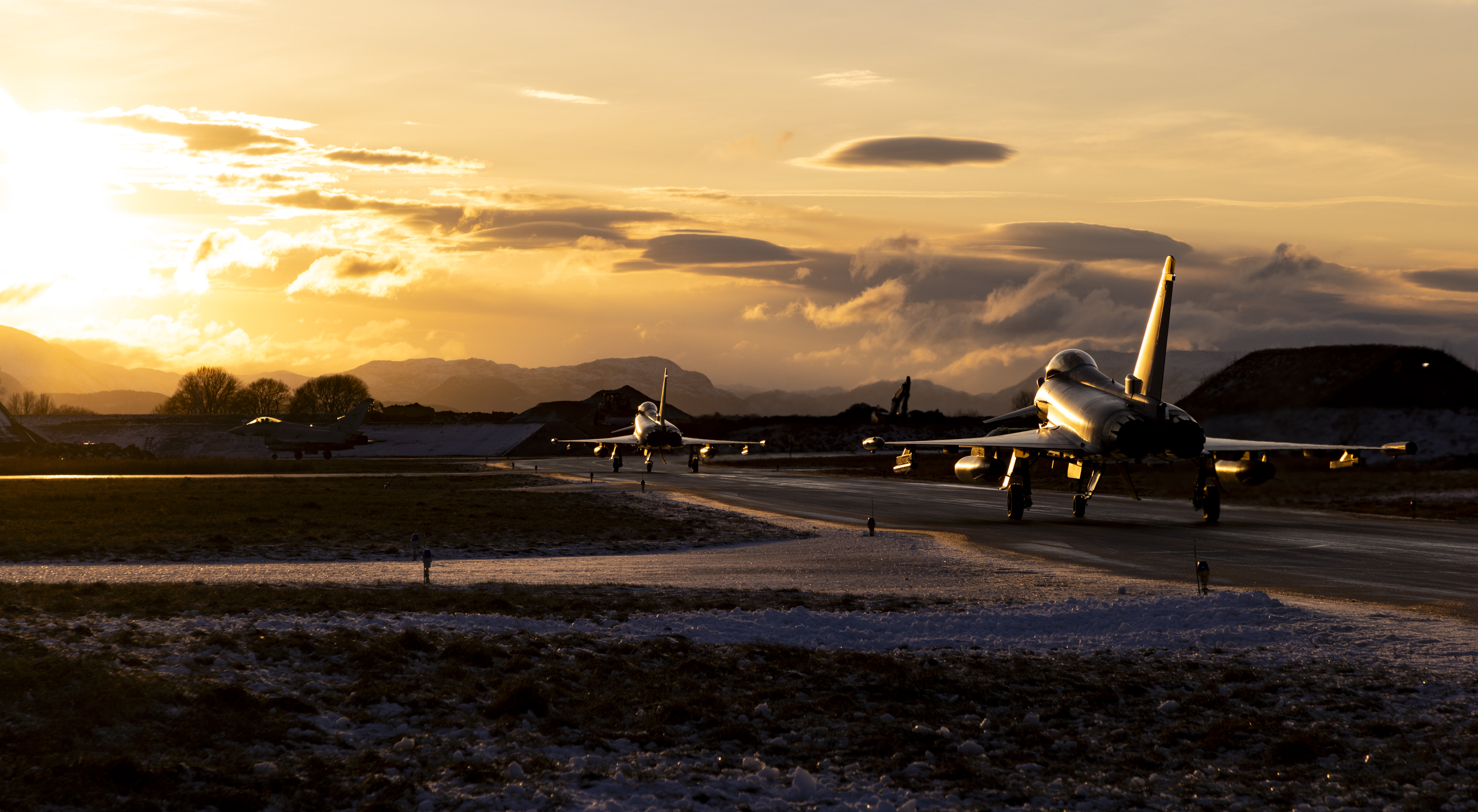 two RAF Typhoons taxing away in a snow covered landscape at sunset
