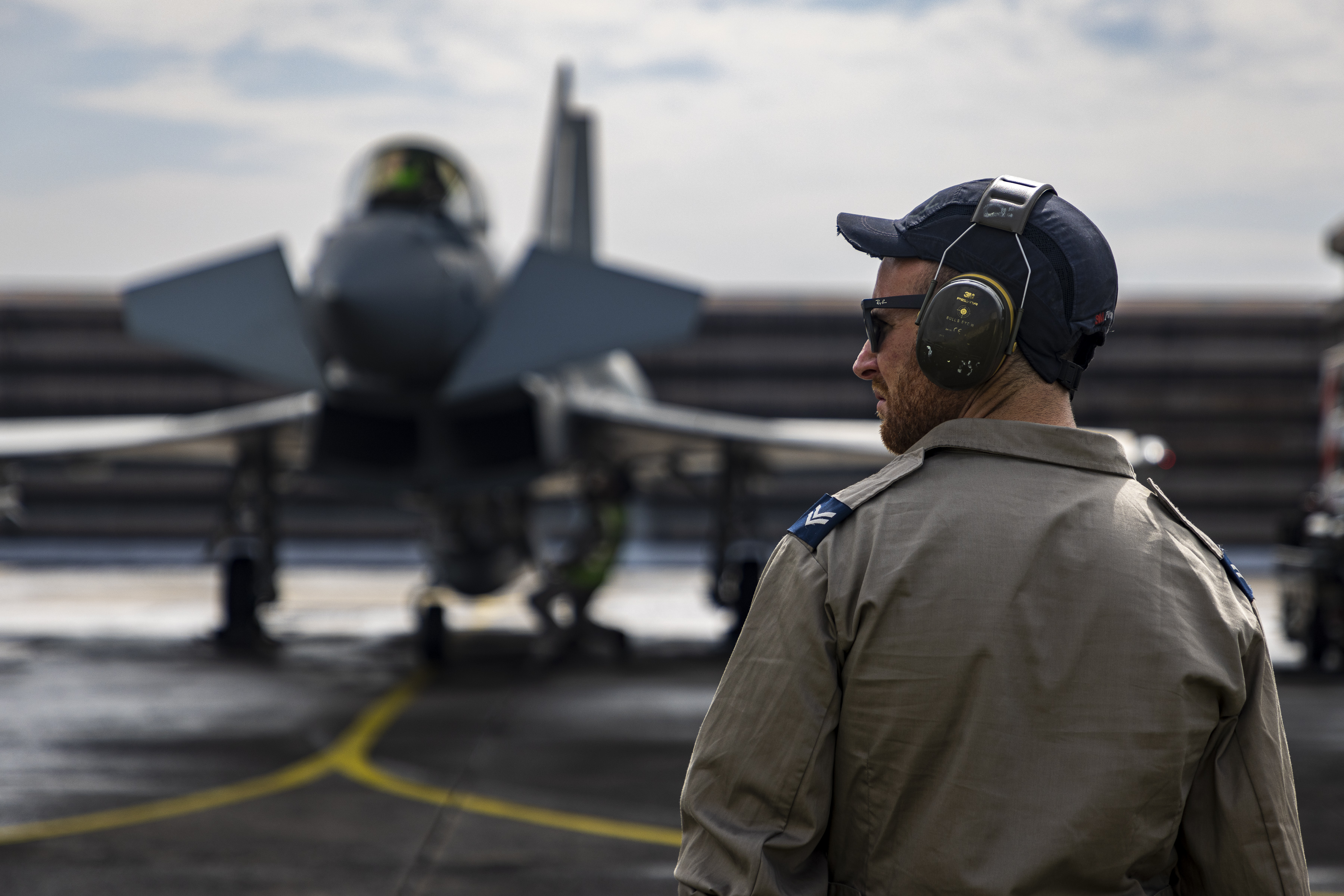 RAF engineer stood on runway with ear protection, directing a taxiing typhoon aircraft