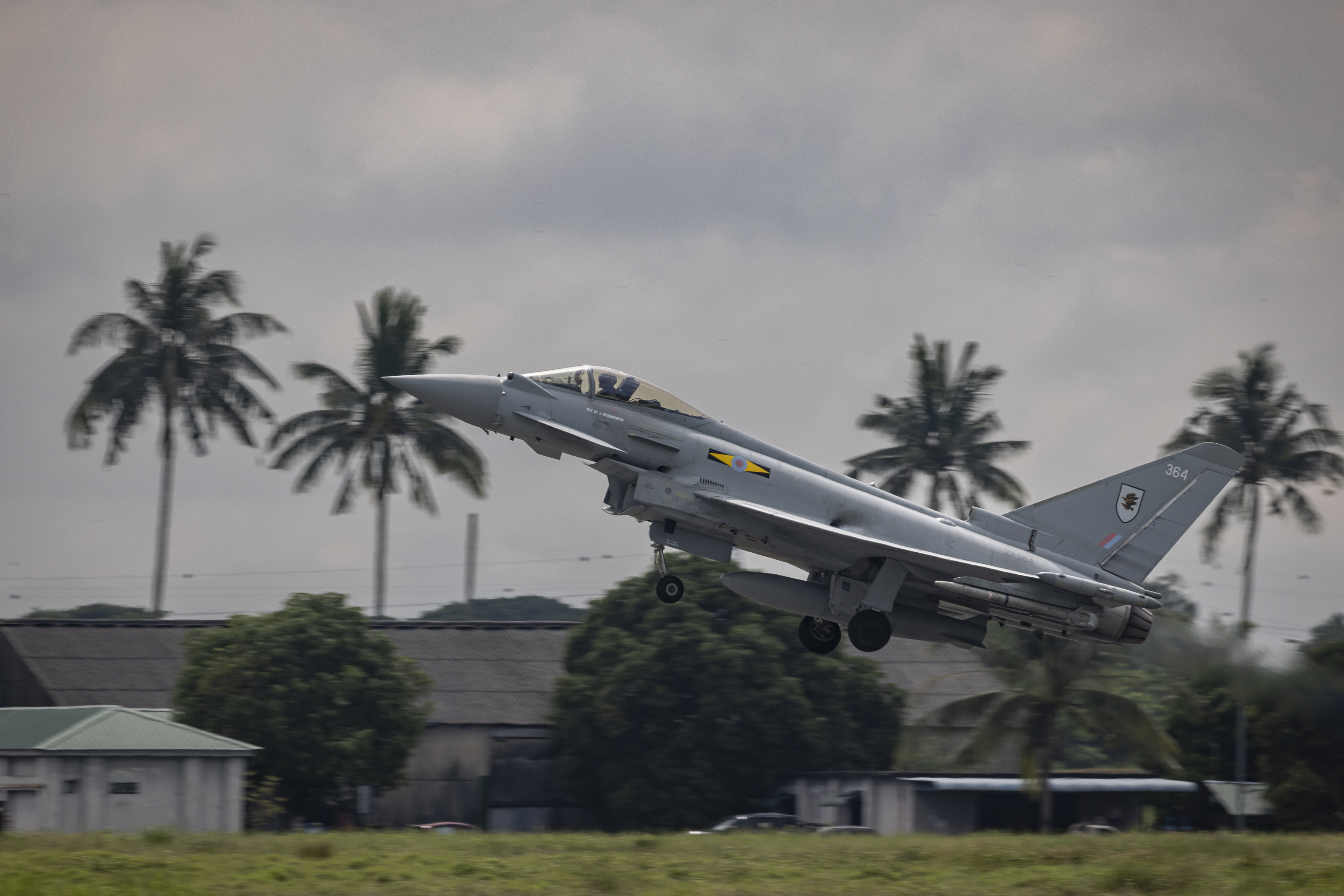 military aircraft taking off from runway with palm trees in background
