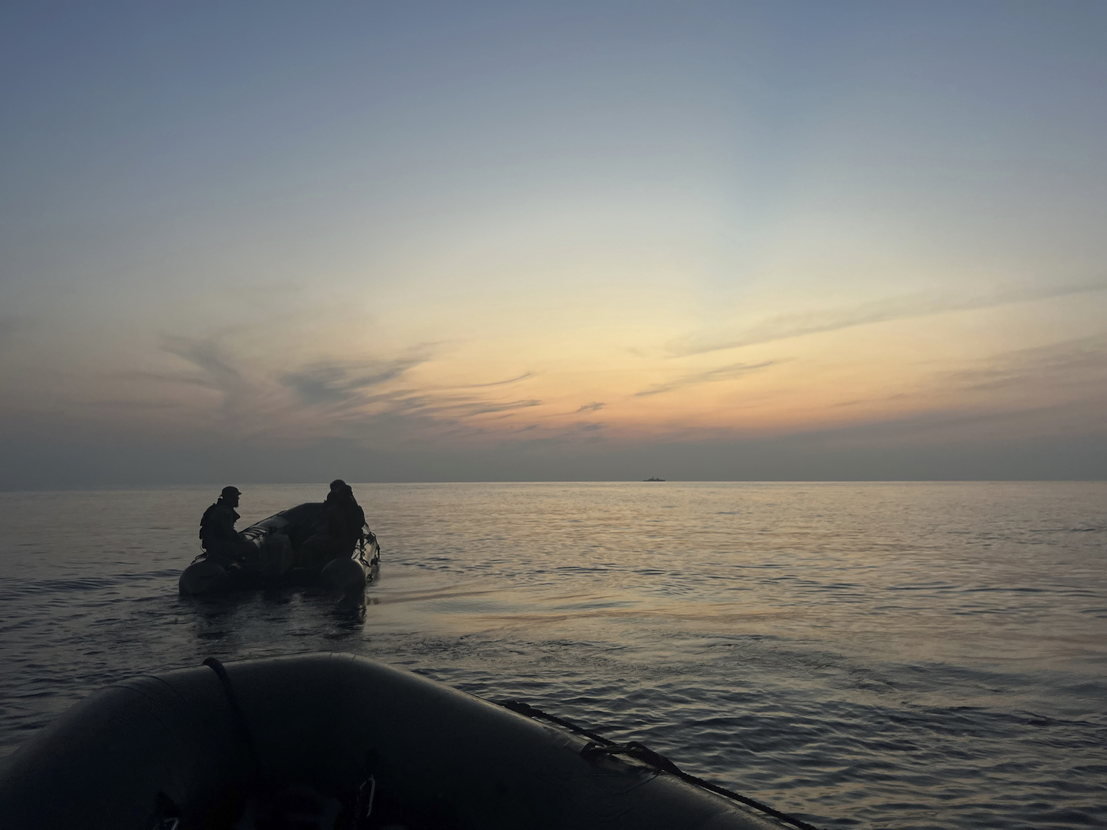 small boat and military personnel on the ocean at sunset