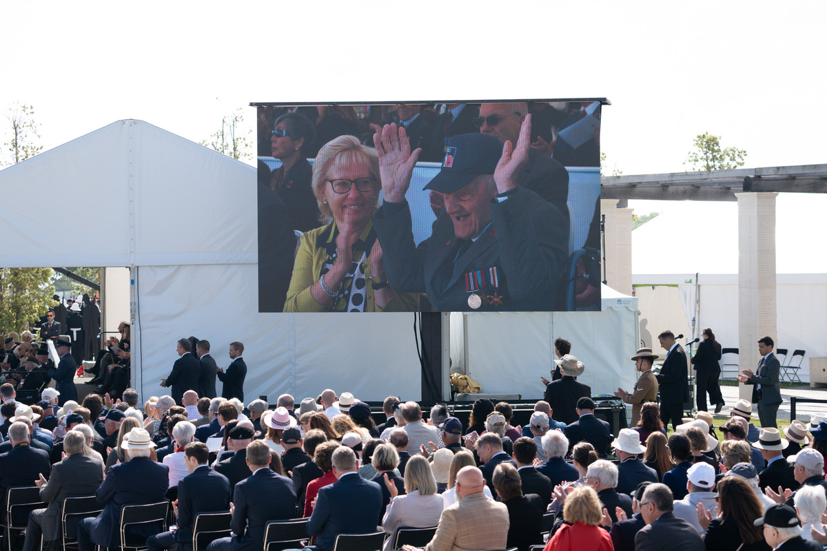 A veteran shown with his hands in the air on a big screen at the event.
