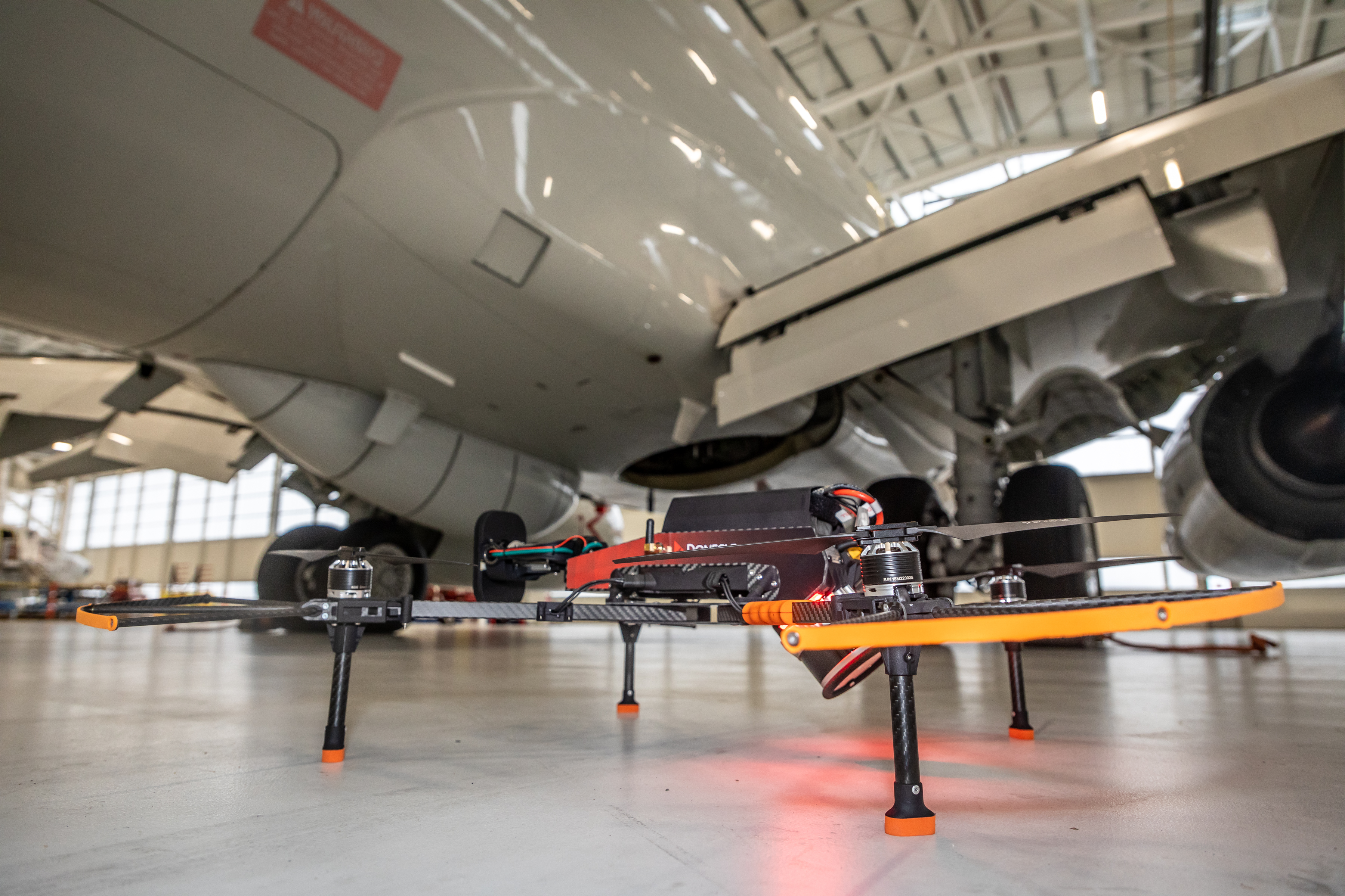 Picture shows a drone on the floor of a hangar in front of an aircraft