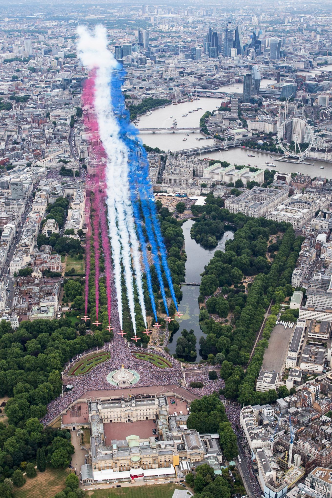 The Red Arrows fly over Buckingham Palace in formation with red, white and blue smoke plumes trailing behind.