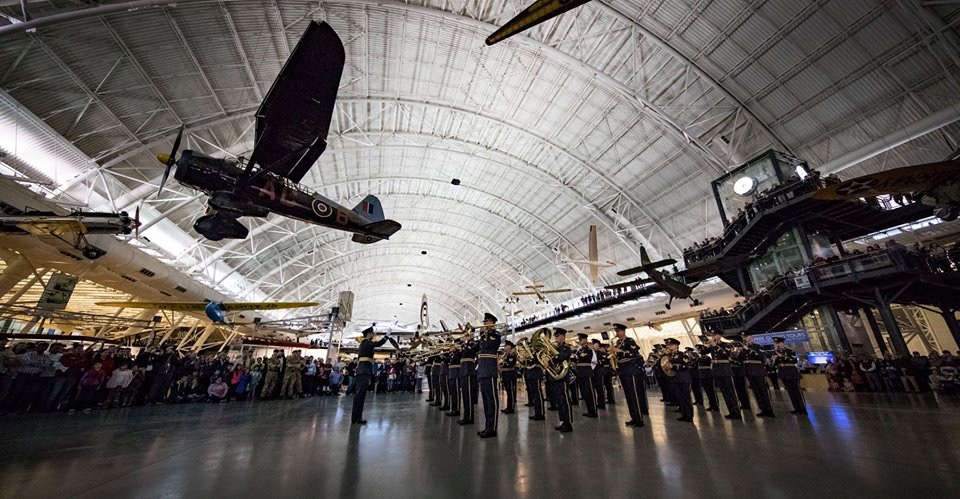 Central Band of the RAF parade beneath aircraft suspended from the ceiling of the hangar.