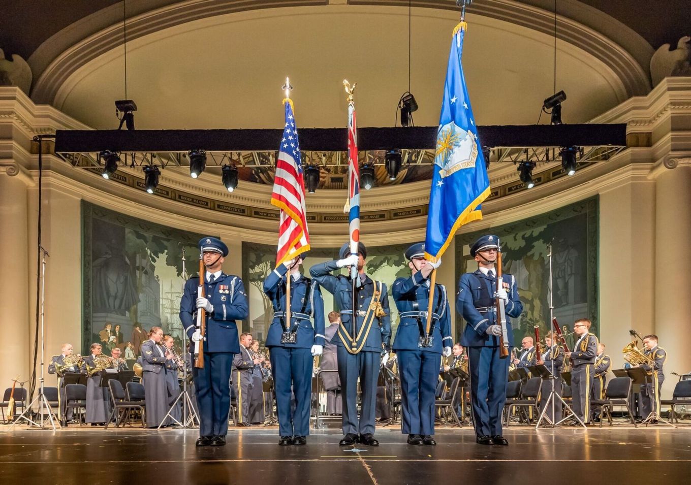 Five officers stand on a stage with flags and insignia.