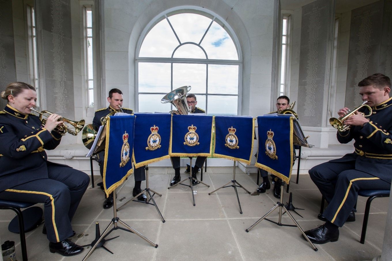 Brass Quintet play music infront of a lage arched window.