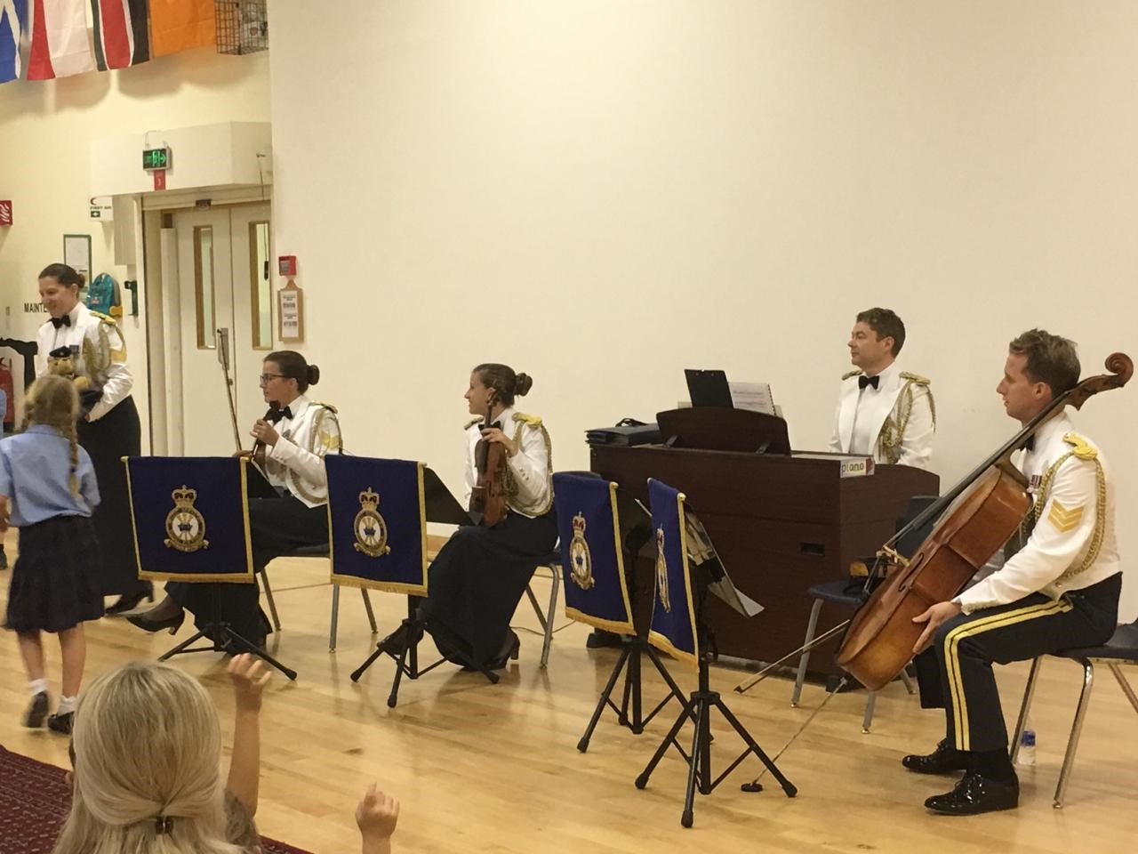 Musicians in uniform introduce their next piece of music to children.