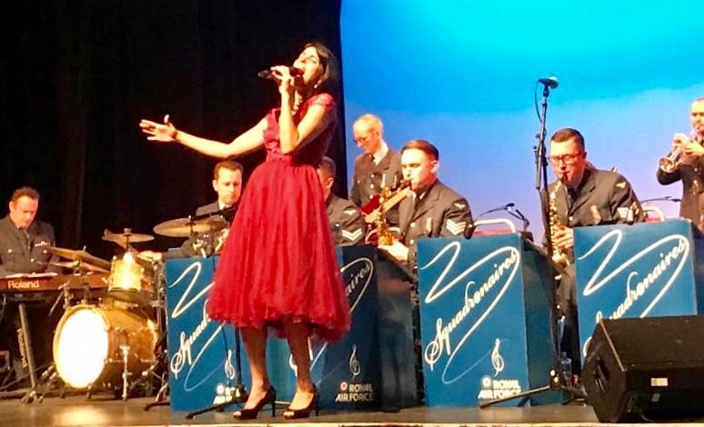 Vocalist in a red dress, sings infront of the big band.