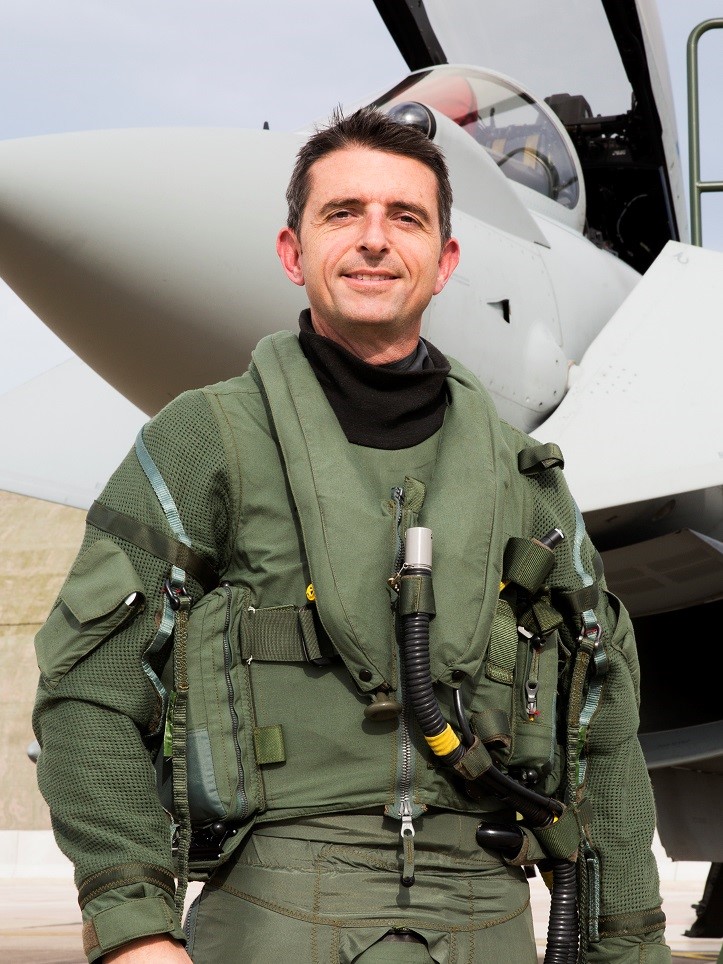 Image shows Air Commodore Paul Godfrey in front of a Typhoon aircraft wearing his flying suit.