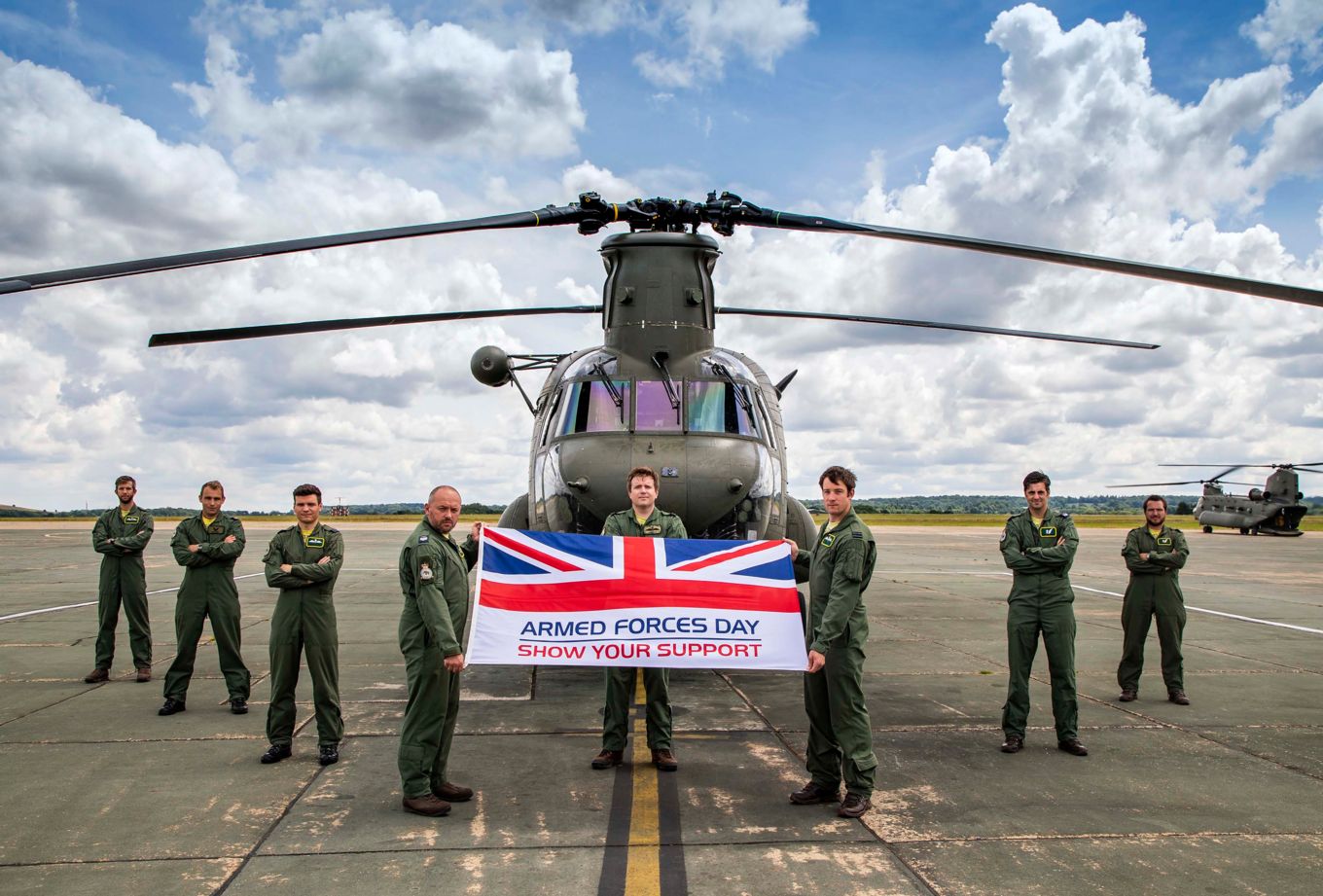 Image shows RAF personnel holding an Armed Forces Day flag standing in front of an RAF Chinook helicopter.