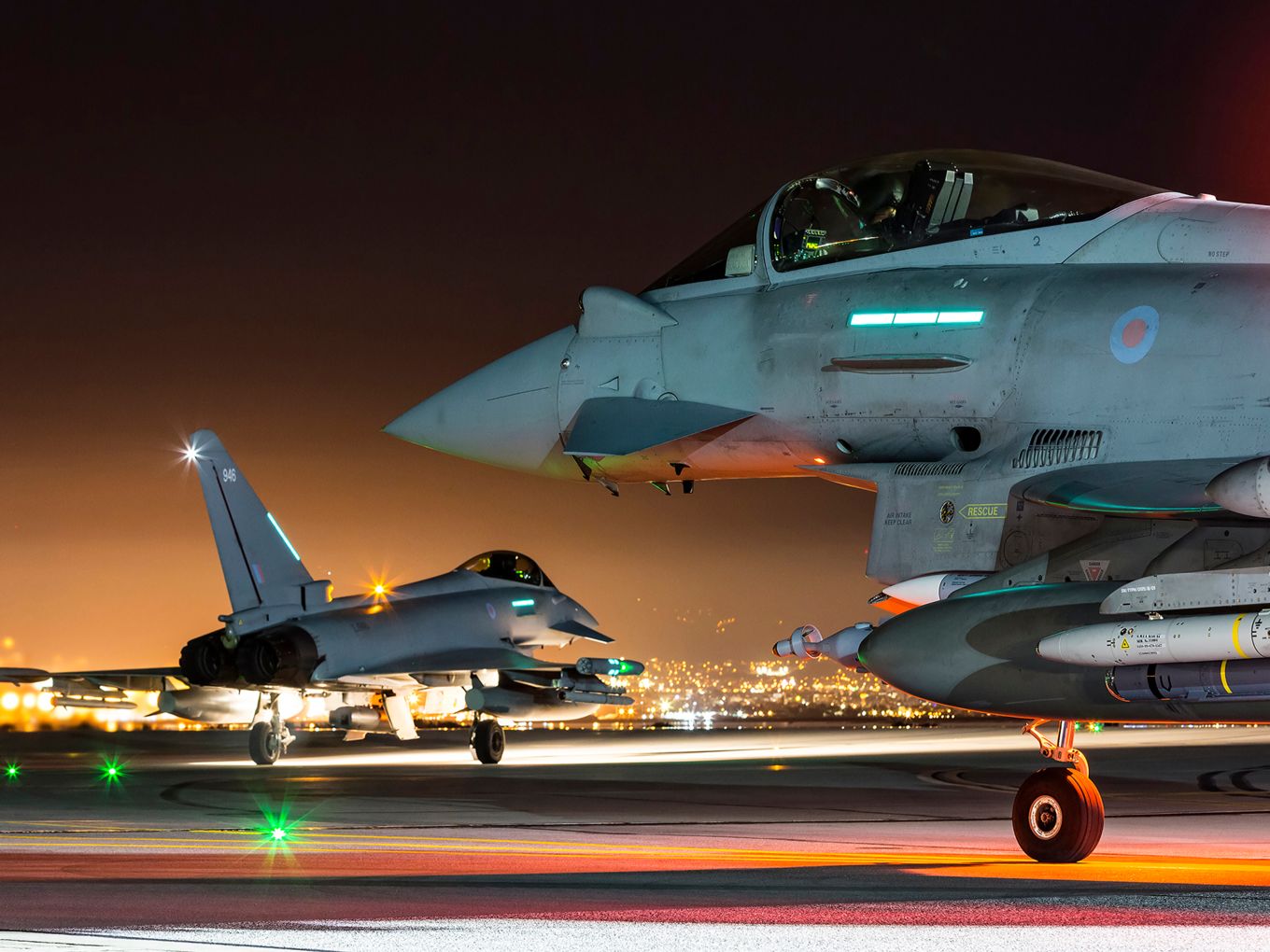Two typhoons on the airfield at night, with lights.