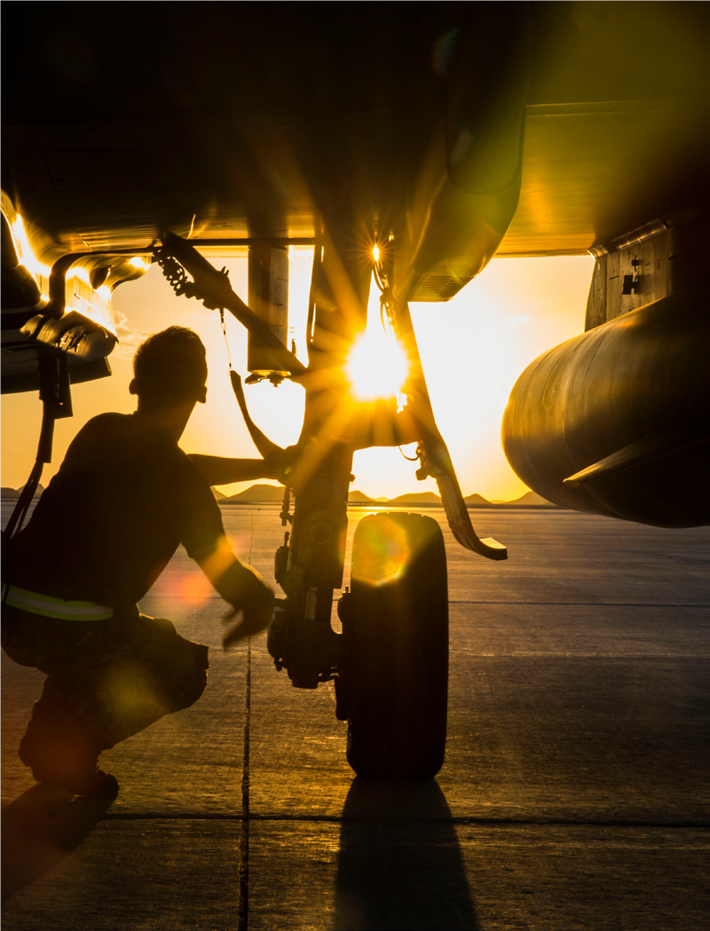 Pilot maintaining aircraft amid sunset.